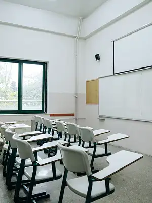 Empty school classroom with rows of student desks, a whiteboard, and a projector screen
