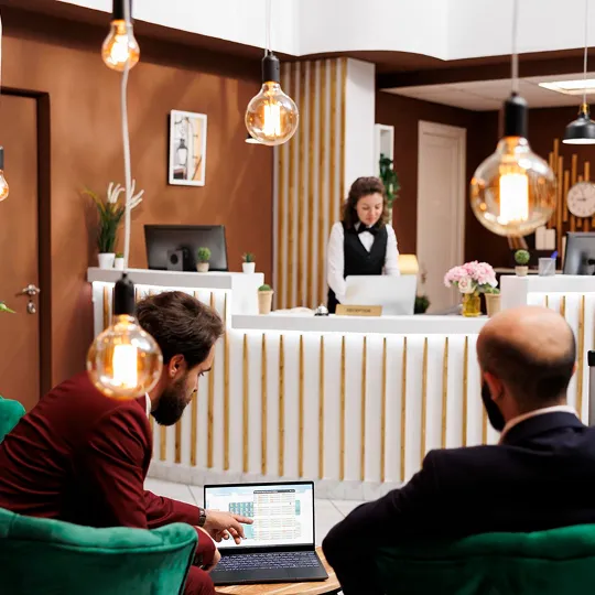 Hotel lobby with a receptionist at the front desk and guests reviewing a laptop in the seating area