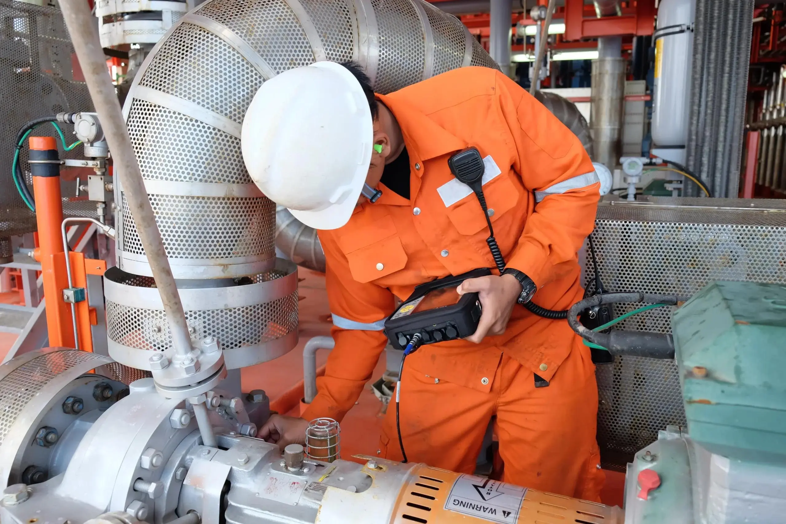 Offshore technician in orange coveralls taking a condition reading on a pump with a handheld meter
