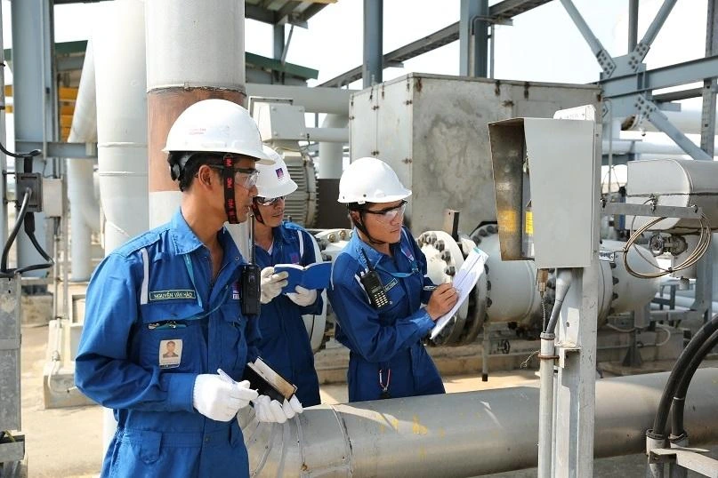 Three technicians in hard hats documenting a pipeline inspection at a gas processing facility