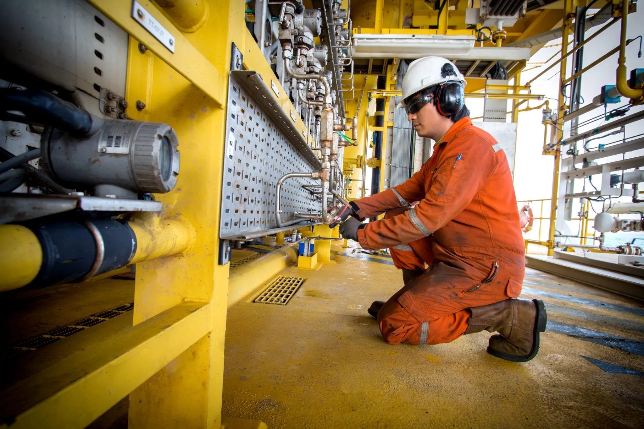 Offshore platform technician in coveralls and hearing protection servicing instrumentation on a process skid