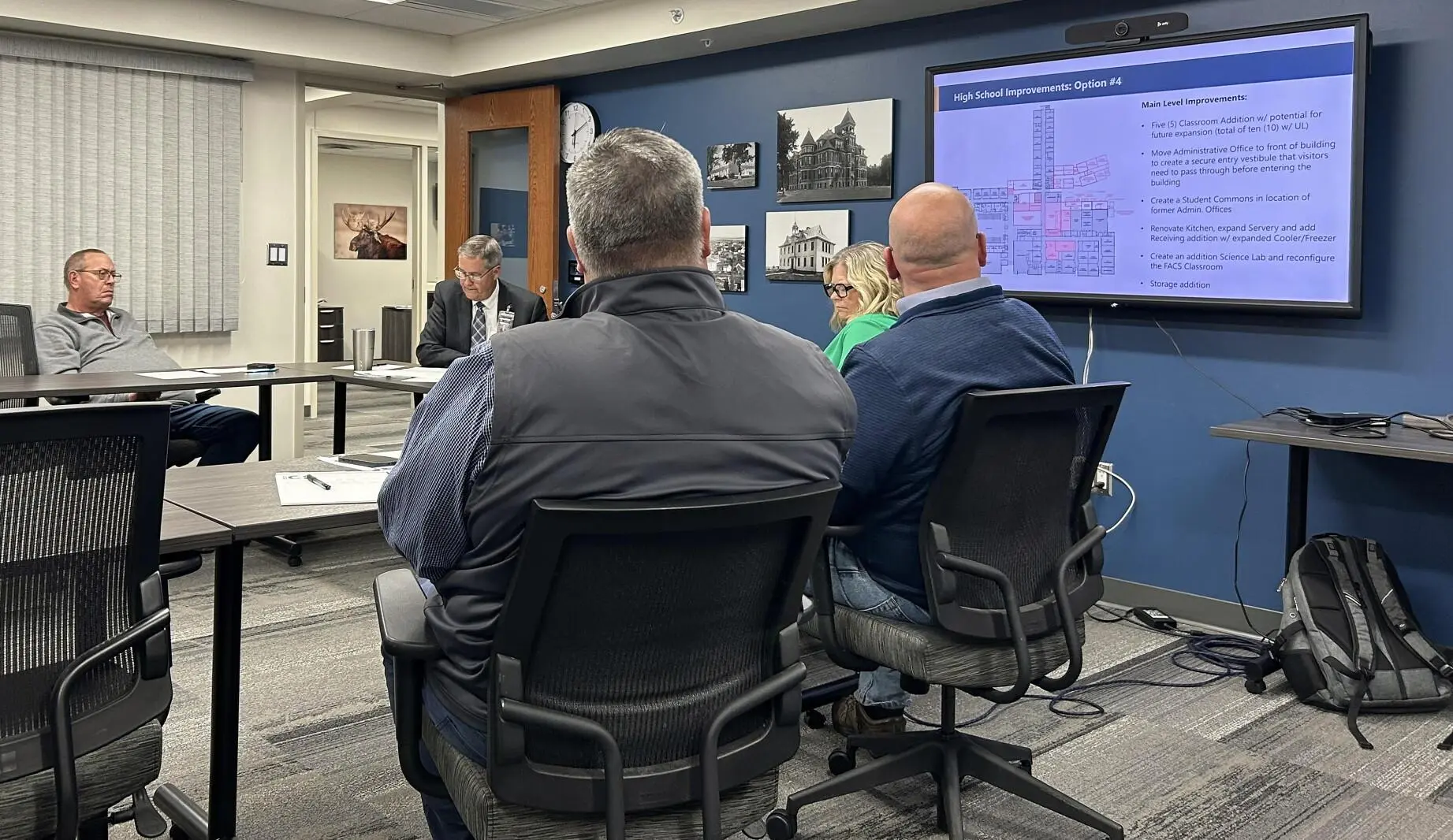 School board members reviewing a high school improvement plan on a screen during a budget meeting