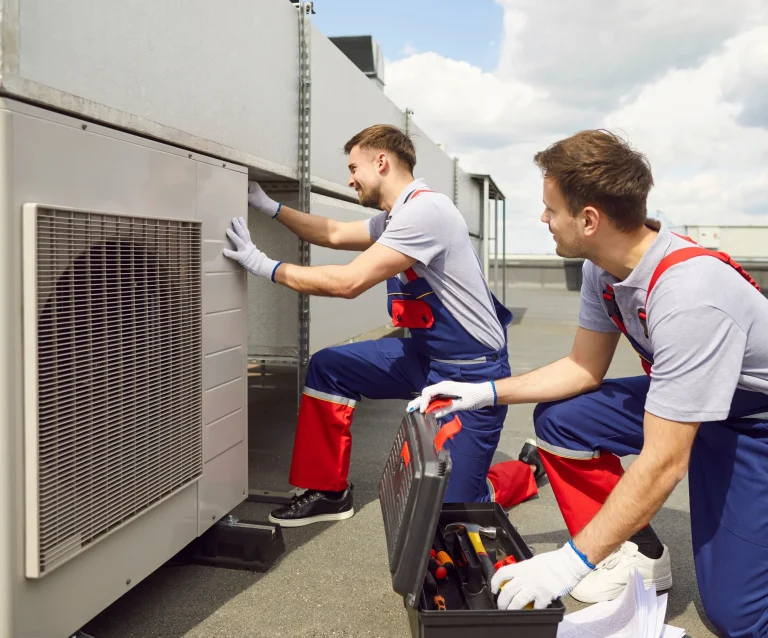 Two HVAC technicians servicing a rooftop condenser unit, the kind of preventive work MPACT CMMS by MPulse Software schedules and records