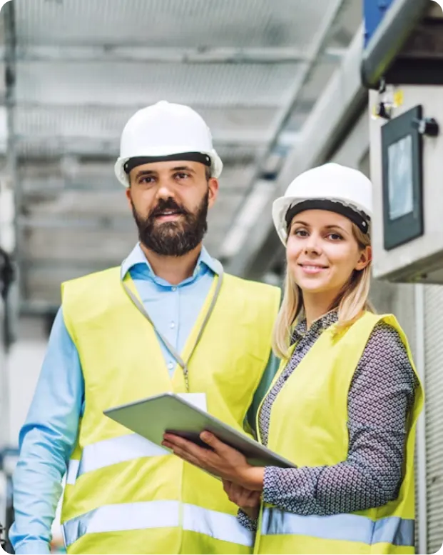 Two maintenance team members in hard hats and safety vests reviewing a tablet on a plant floor
