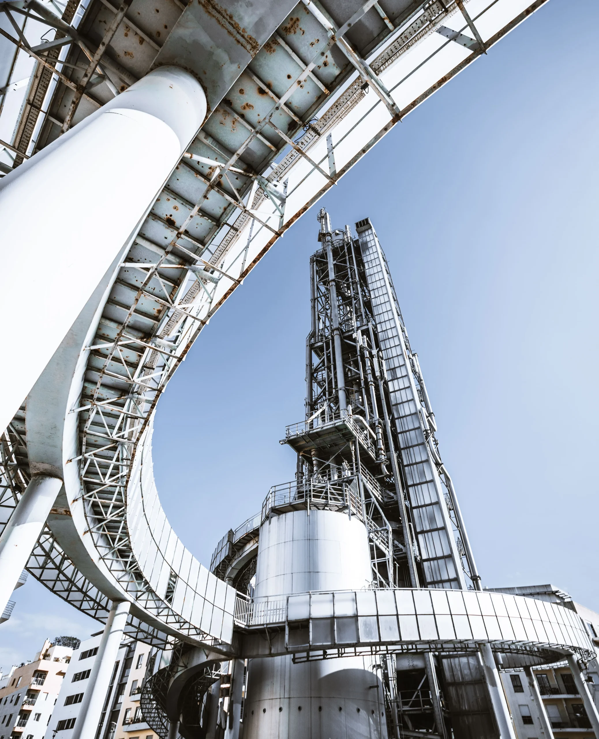 Low-angle view of large ductwork, steel piping, and a process tower at an industrial power facility under a clear sky